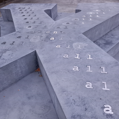 Monument i betong i form av bokstaven X liggande med text på.