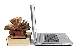 Uppslagen laptop och en trave med gamla böcker.