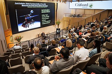 View from the back of a lecture hall showing attendees seated and facing Professor Veerabhadran as he gives a lecture at the front of the room.
