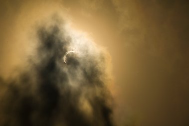 Solförmörkelse med molnslöjor mot gul himmel