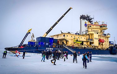 People playing on the ice, with icebreaker Oden in the vackground.