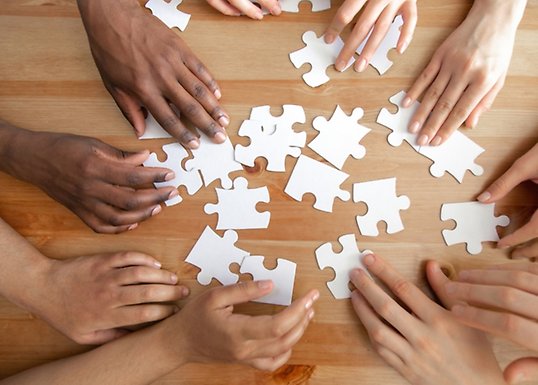 Hands belonging to people of different colours assembling a puzzle on a table.