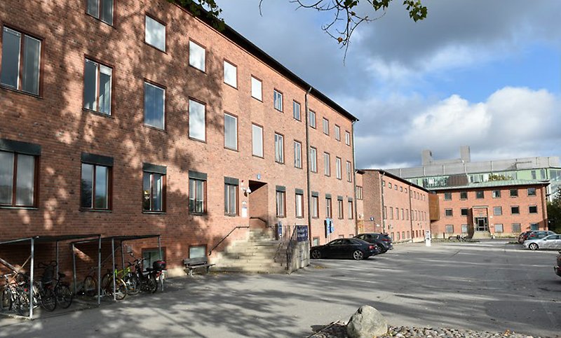 Bruna tegelbyggnad med en parkeringsyta framför.