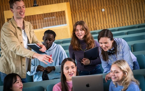 Studenter samlade runt en laptop, pratar och skrattar.