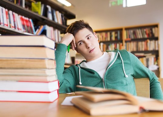 Male student looking at a pile of books, looking tired.