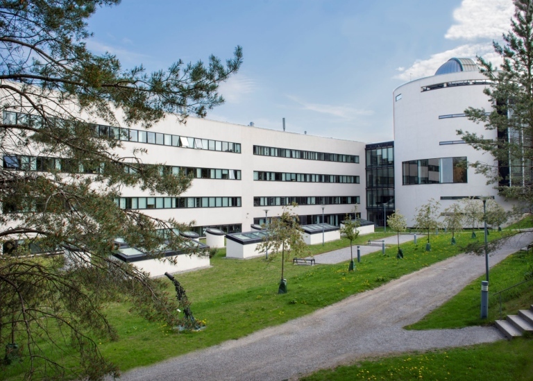 Vit institutionsbyggnad med blå himmel och grön gräsmatta framför.