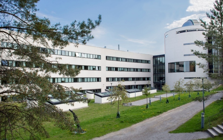 Vit institutionsbyggnad med blå himmel och grön gräsmatta framför.